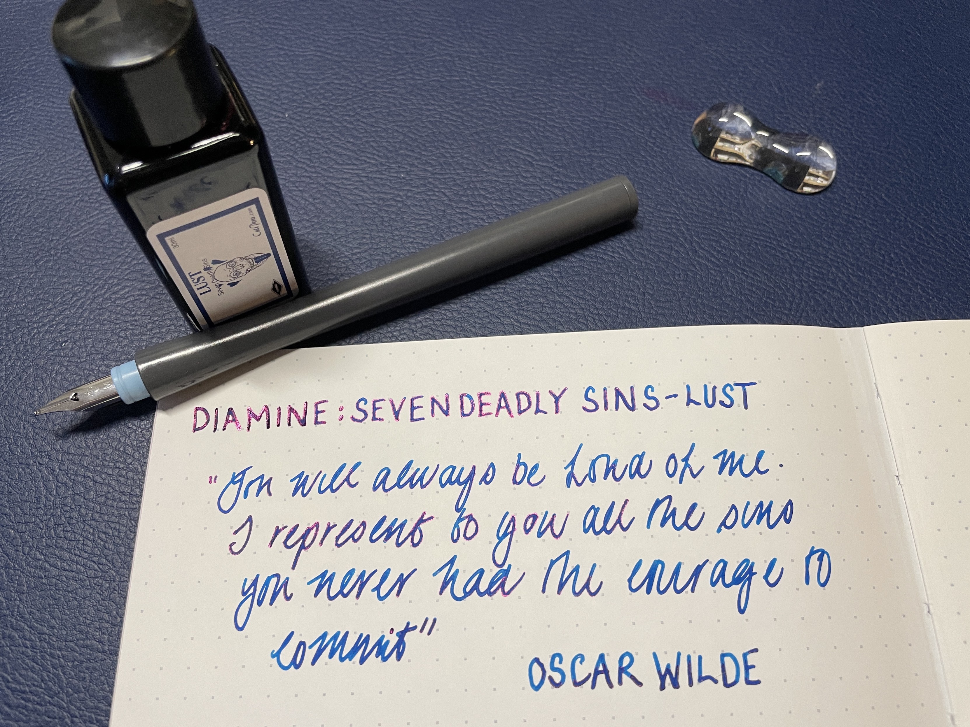 Open notebook with handwritten quote, dip pen, ink bottle, and pen rest on a blue surface.